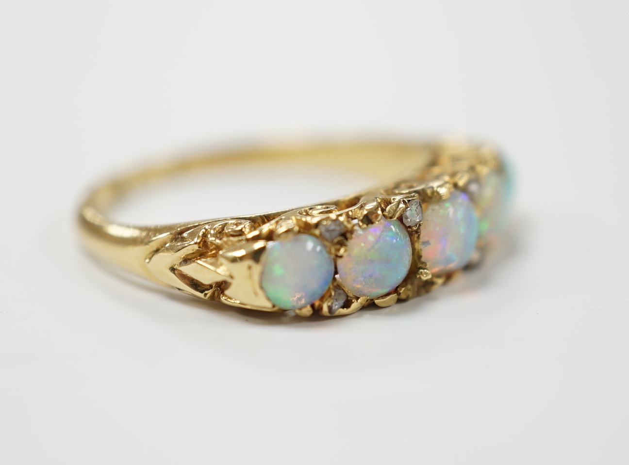 A late Victorian yellow metal and white opal five stone ring with diamond chip set spacers, size M